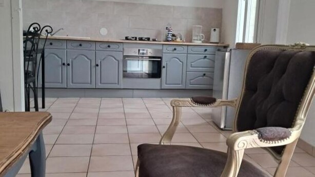Une cuisine avec des meubles de couleur grise, un plan de travail en bois et un coin repas avec une chaise.