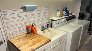 Un área de lavandería con encimera de madera, lavadora, secadora y estante con productos de limpieza.