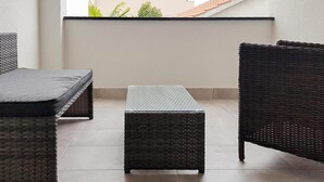 Un balcón con mobiliario de mimbre, que incluye una silla y una pequeña mesa.