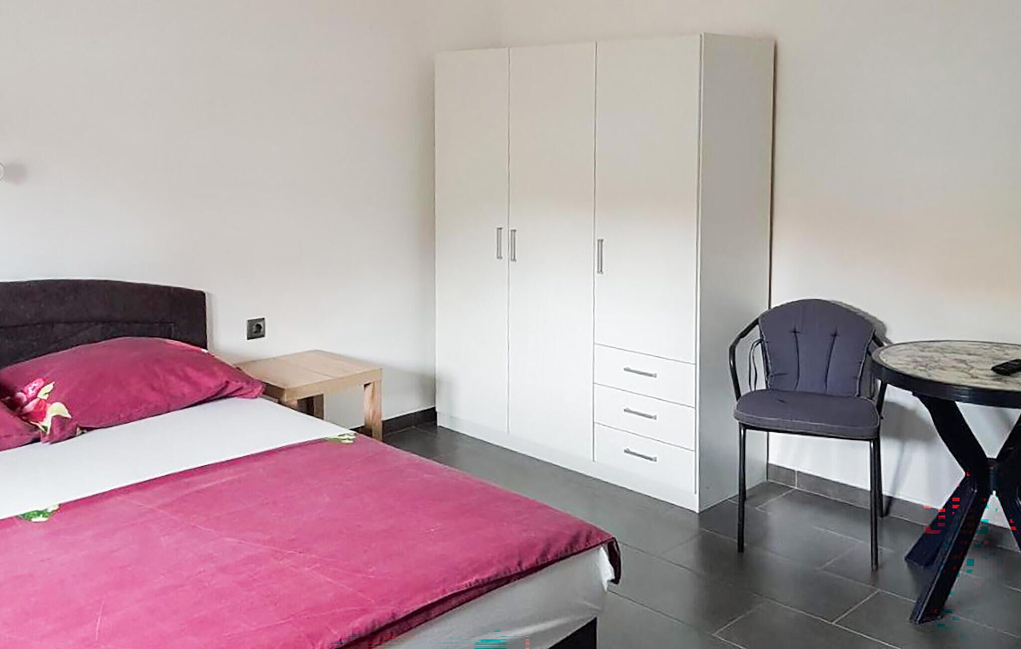 Une chambre à coucher avec un lit, une petite table, une chaise et une armoire.