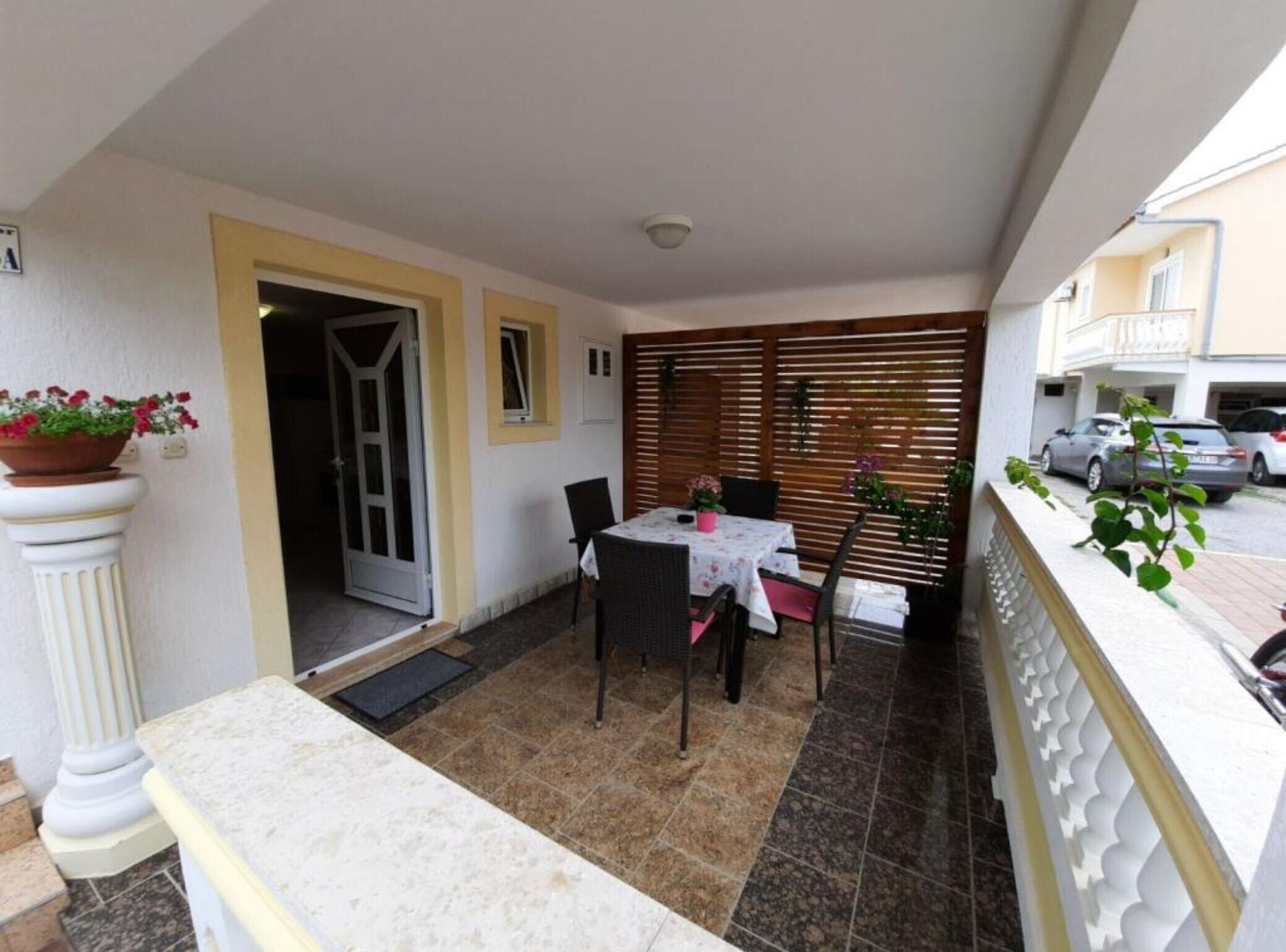 A small patio with a table and chairs, a potted plant, and a sliding door leading to a room.
