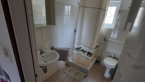 Et badeværelse med vask, toilet og bruseforhæng.