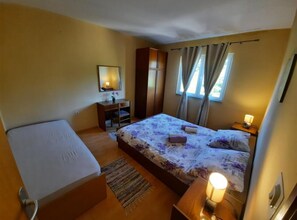 Une chambre à coucher comprenant un lit, un bureau, une armoire, un miroir et une fenêtre avec des rideaux.