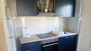 Pieni, käytännöllinen keittiö, jossa on tummansiniset kaapit, valkoinen työtaso, kahvinkeitin ja pesuallas.