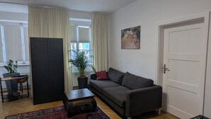 En moderne stue med sofa, to tæpper, et sofabord, en potteplante og et billede på væggen.