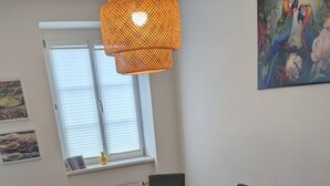 Et rundt spisebord med seks stole, en vase med plante og et billede på væggen.