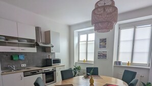 Et moderne køkken med hvide skabe, en mikroovn og en komfur. Der er et spiseområde med et rundt bord og stole, samt en hængende lampe.