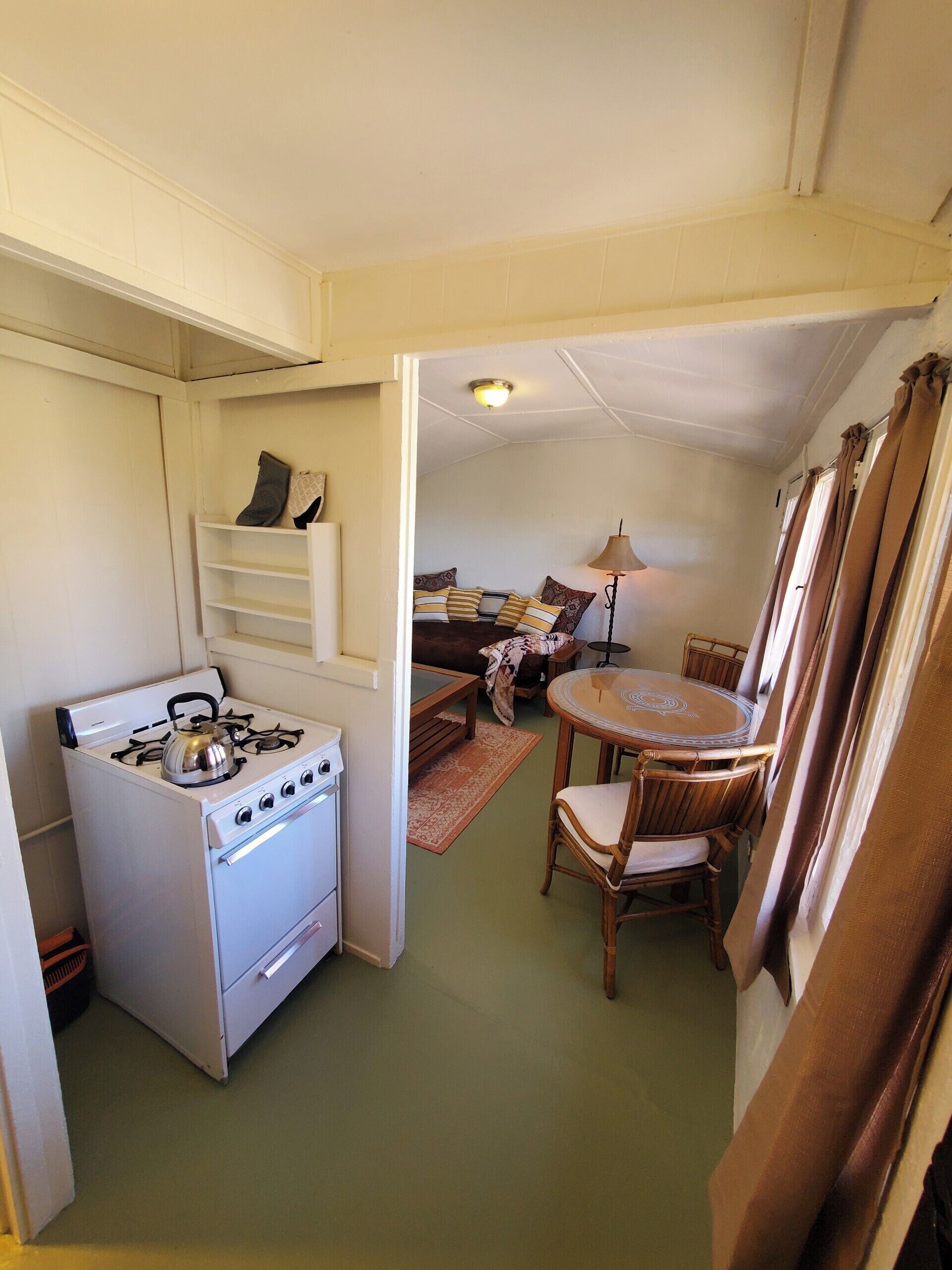 A compact kitchen with a stove, a dining table with chairs, and a small seating area with a sofa and a lamp.