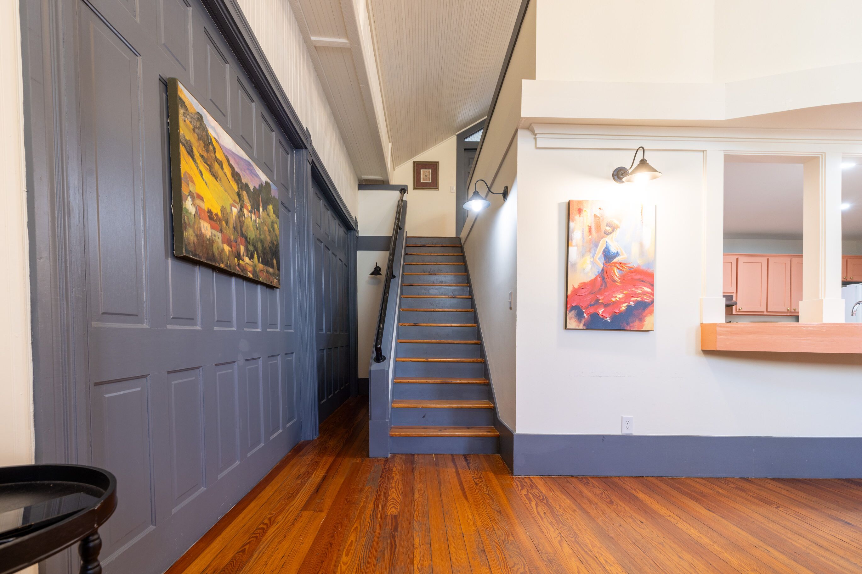A staircase with wooden steps and a handrail, leading to a landing with a painting and a light fixture.