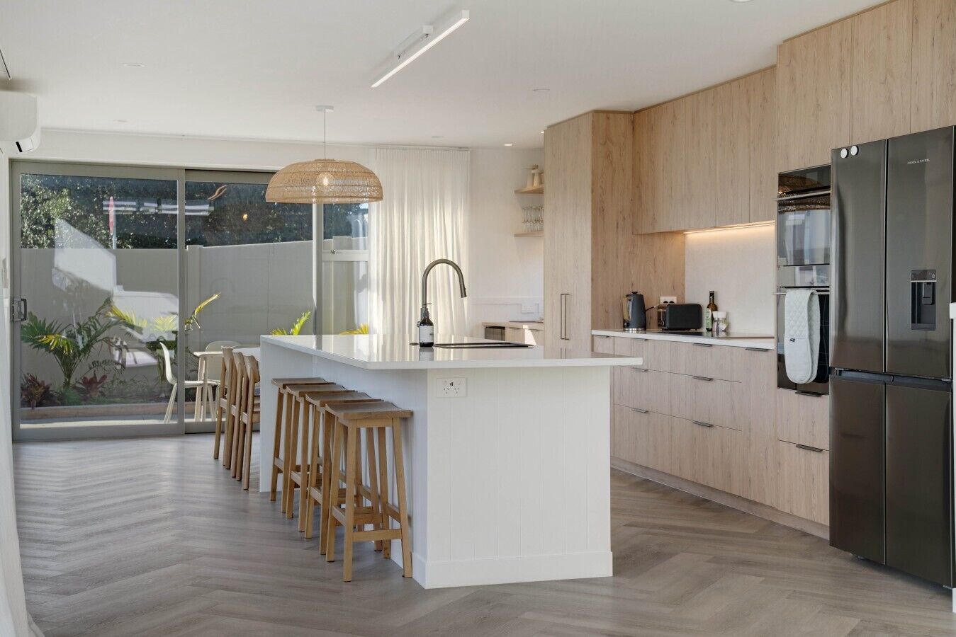 Una cocina moderna con una isla central, taburetes de madera y un refrigerador de acero inoxidable.