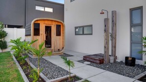 Un edificio moderno con sauna de madera, patio de hormigón y jardín minimalista.