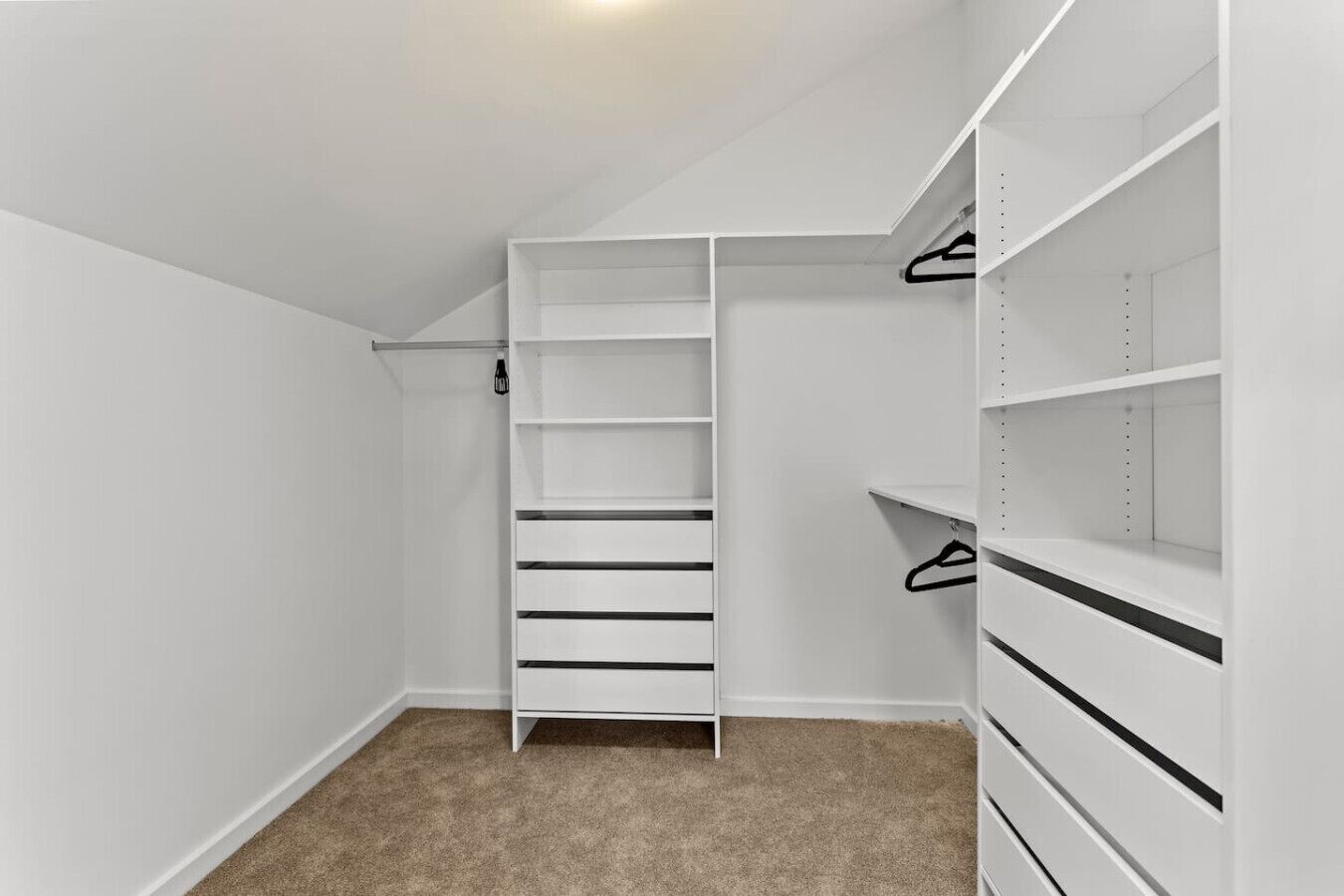 A walk-in closet with open shelving and hanging space, carpeted floor, and white walls.