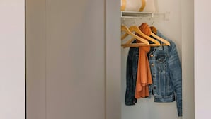 A closet with a hanging rack holding a denim jacket and an orange garment. - Studio Queen Apartment (Detroit)