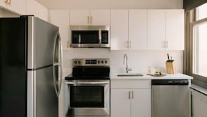 A modern kitchen with stainless steel appliances, white cabinetry, and a dishwasher. - Studio Queen Apartment (Detroit)