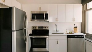 A modern kitchen with stainless steel appliances, white cabinetry, and a dishwasher.