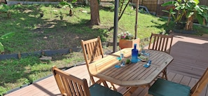 Eine Holzterrasse mit Tisch und Stühlen, umgeben von Grünpflanzen und einem Holzzaun.
