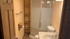 Un baño con puerta de madera, inodoro blanco, cabina de ducha con mampara de vidrio y lavamanos de mármol.