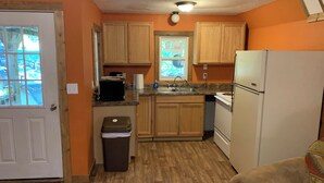 Una cocina compacta con armarios de madera, un refrigerador, un lavamanos y un bote de basura.