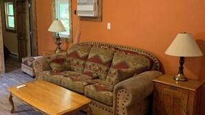 Una sala de estar acogedora con una mesa de centro de madera, un sofá estampado y dos lámparas sobre mesitas de noche de madera.