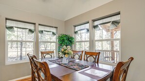 A dining room with a wooden table, four chairs, a vase with flowers, and large windows with curtains. - Peaceful Blue Ridge Cabin w/ Wraparound Deck! (Blue Ridge)