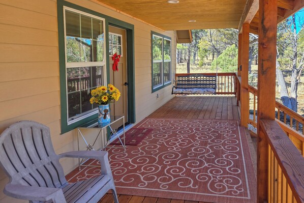 A wooden deck with a patterned rug, a chair, and a table with a vase of flowers. - Peaceful Blue Ridge Cabin w/ Wraparound Deck! (Blue Ridge)
