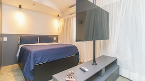Ein Hotelzimmer mit Bett, Flachbildfernseher, einem kleinen Tisch mit Fernbedienung und einem dekorativen Gegenstand.