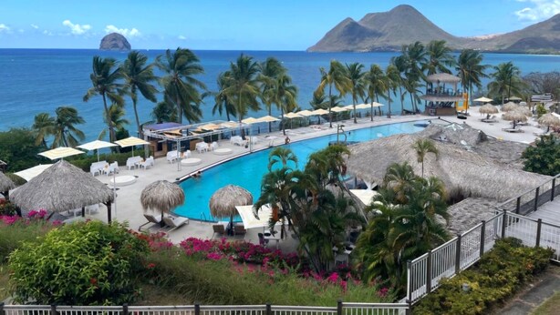A resort pool area with a clear view of the ocean, palm trees, and a mountain in the background. - A tropical break, facing the Caribbean Sea in an exceptional setting (Le Diamant)