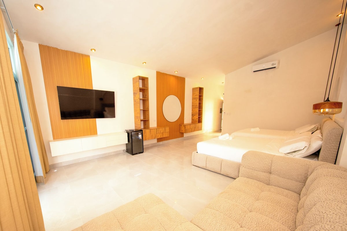 Une chambre d’hôtel moderne avec un grand lit, un canapé, une télévision et des étagères en bois intégrées.