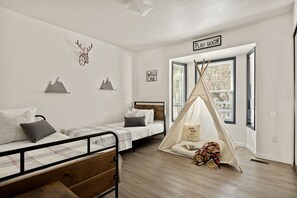 Una habitación con dos camas, un letrero que indica sala de juegos, un letrero que dice 'salvaje', una decoración con cabeza de ciervo e incluso un tipi.