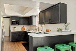 Una cocina moderna con armarios oscuros, una encimera blanca, un microondas integrado y un taburete verde.
