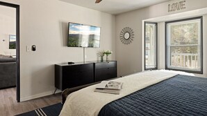 Ein Schlafzimmer mit einem Bett, einem Deckenventilator, einem Fernseher, einer Kommode und einem Fenster mit Jalousien.