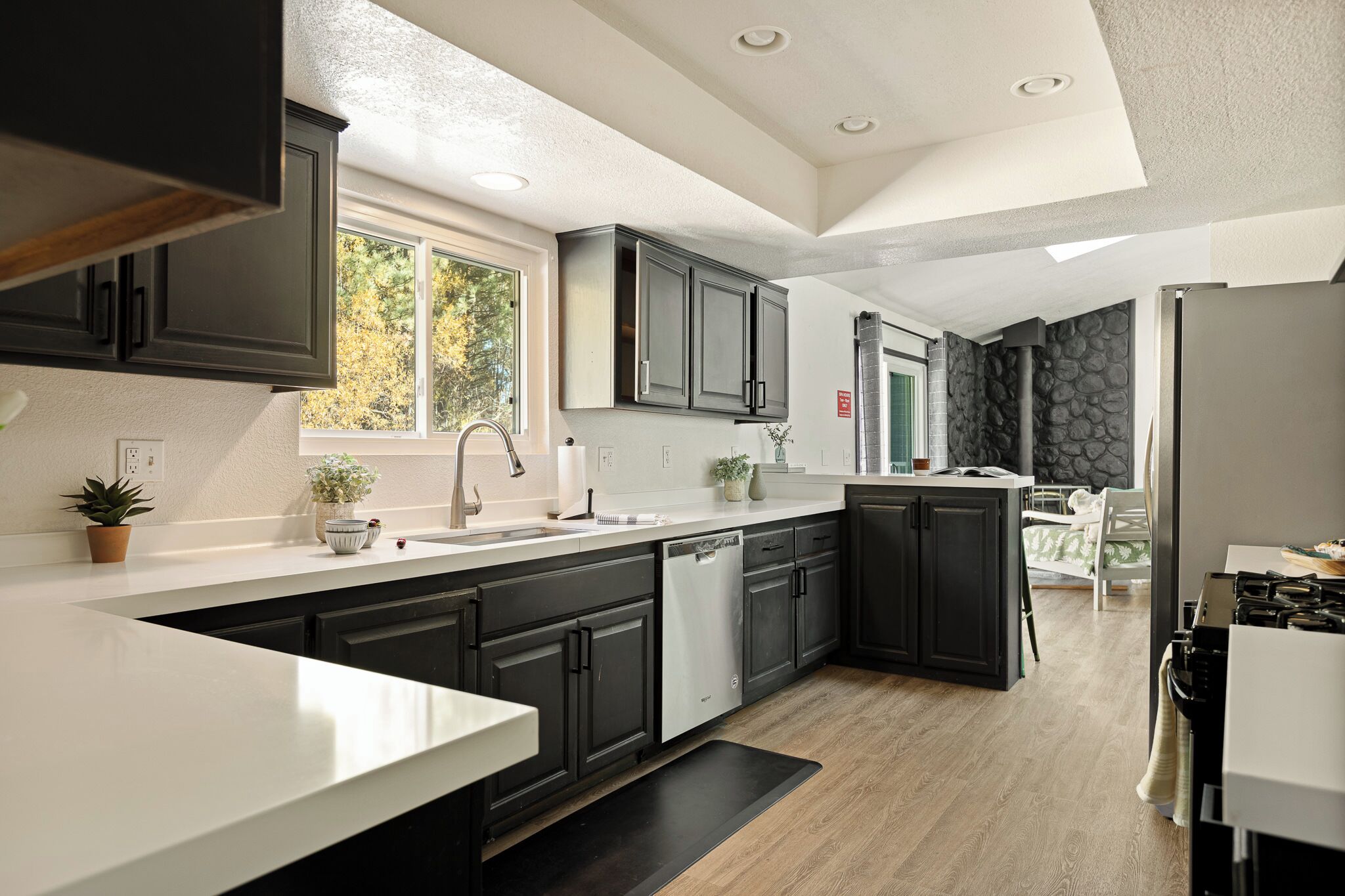 A modern kitchen with dark cabinetry, a white countertop, and a view of the outdoors.