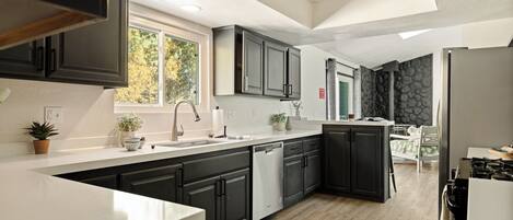A modern kitchen with dark cabinetry, a white countertop, and a view of the outdoors.