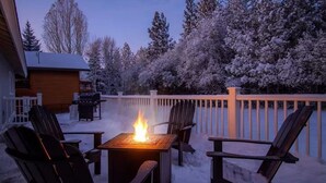 Ein mit Schnee bedeckter Deck mit Feuerstelle und Stühlen.