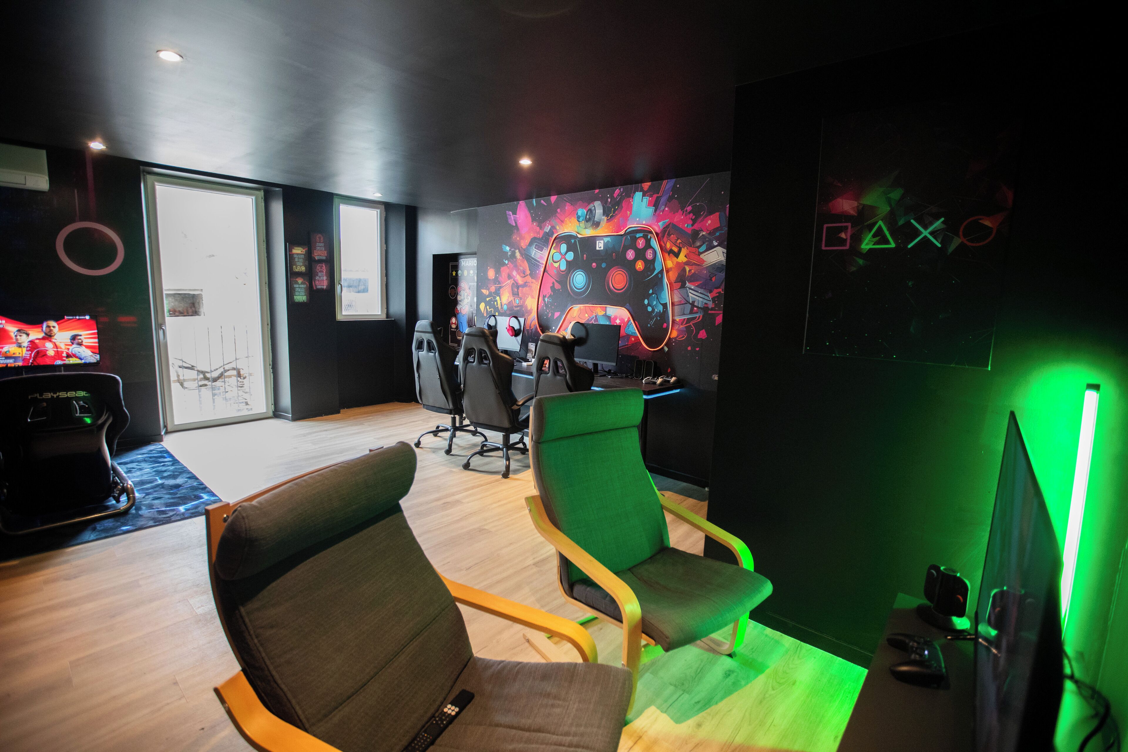 A gaming room with two gaming chairs, a large screen, and a wall with a colorful design.