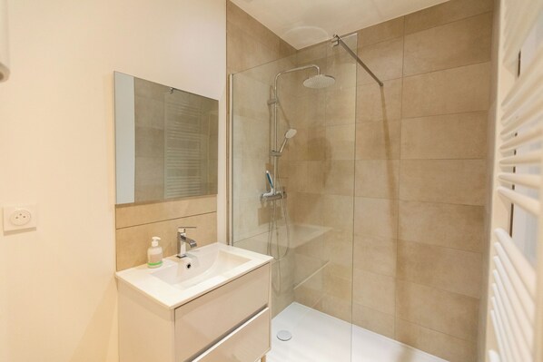 A modern bathroom with a glass-enclosed shower, a white sink, and a mirror above it.