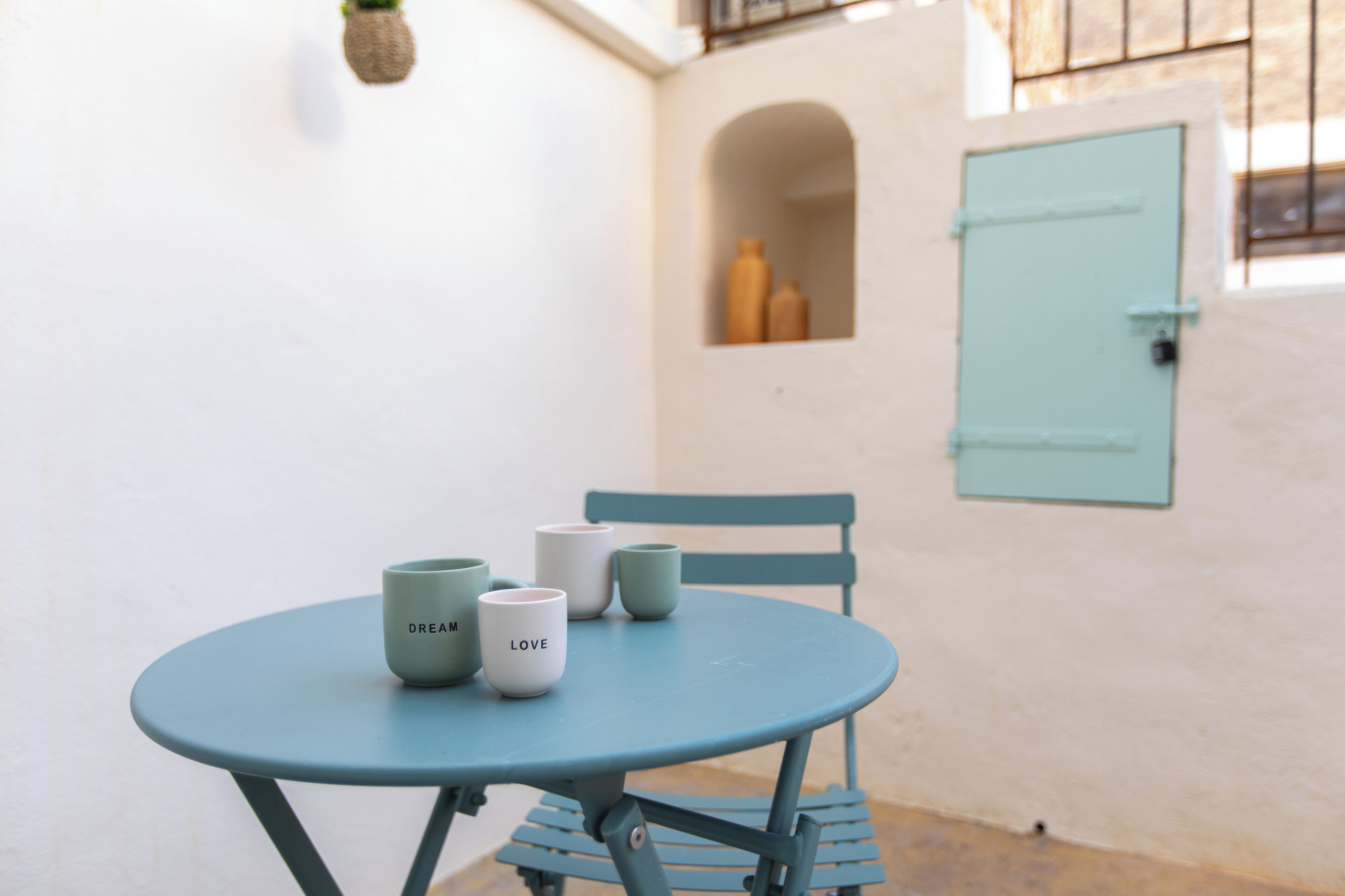 A small round table with four cups, a chair, and a light blue door in a white-walled room.