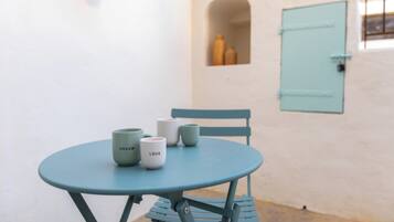 A small round table with four cups, a chair, and a light blue door in a white-walled room.