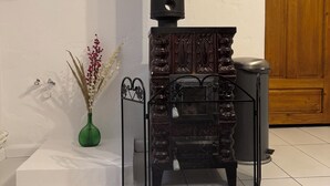 A wood stove with a chimney, a decorative vase, and a wooden cabinet in a room with white walls and tiled flooring.