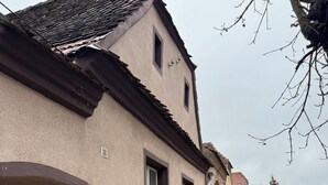 A cobblestone street with a building featuring a wooden door and a window with a brown frame.