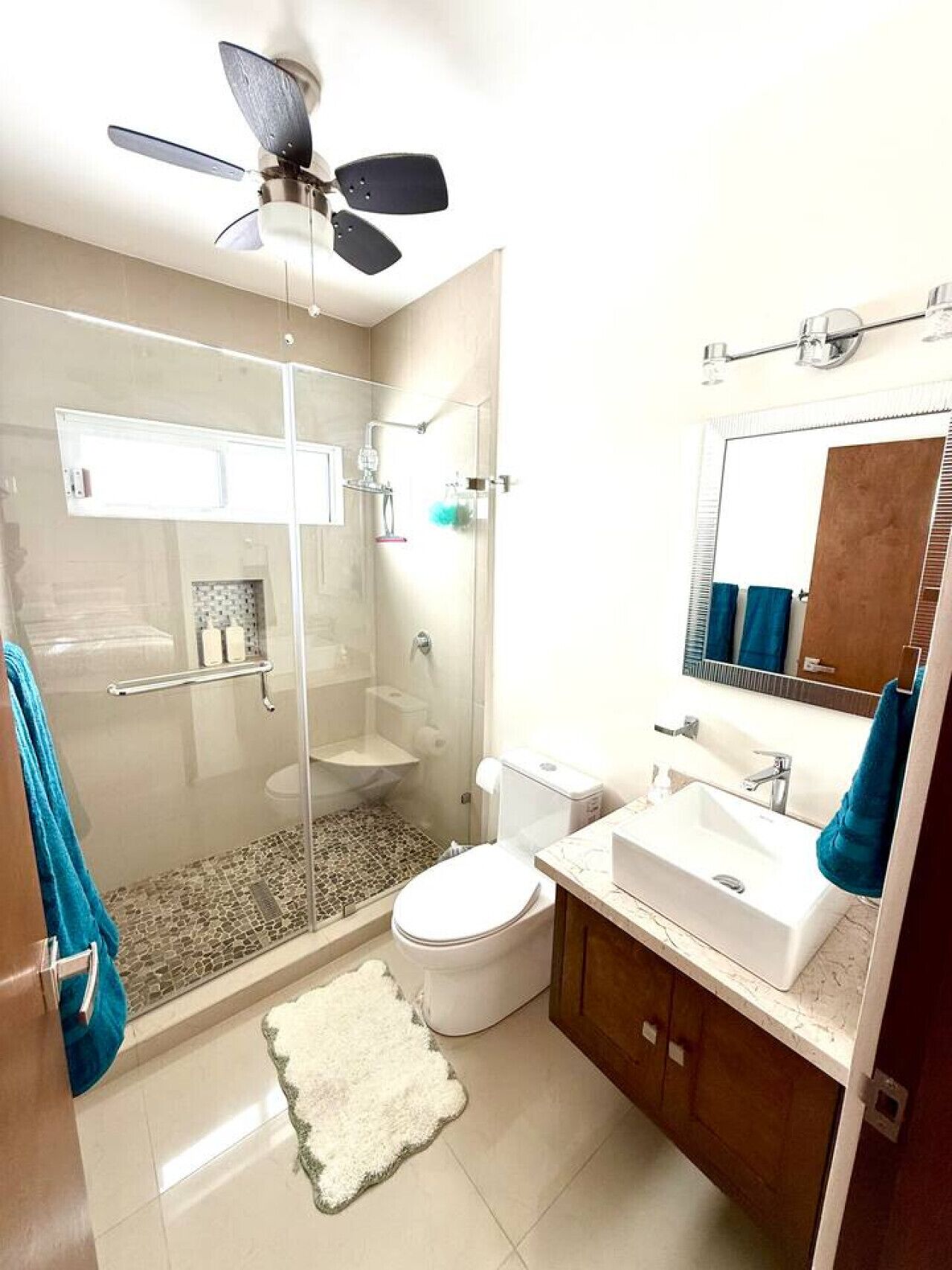 A modern bathroom with a glass-enclosed shower, a toilet, a sink, and a ceiling fan.