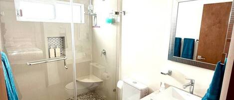 A modern bathroom with a glass-enclosed shower, a toilet, a sink, and a ceiling fan.
