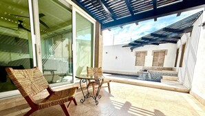 An outdoor patio area with wicker furniture, a glass table, and a view of a pool and building in the background. - Villa Alberca, Bar y Terraza Privada (La Paz)