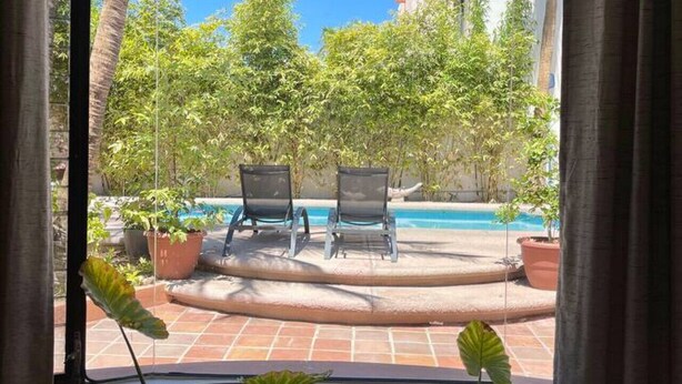 A room with a view of an outdoor pool area, two lounge chairs, and a potted plant. - Water & Flower House (La Paz)