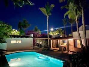 Piscina rodeada de palmeras y un edificio con terraza cubierta.
