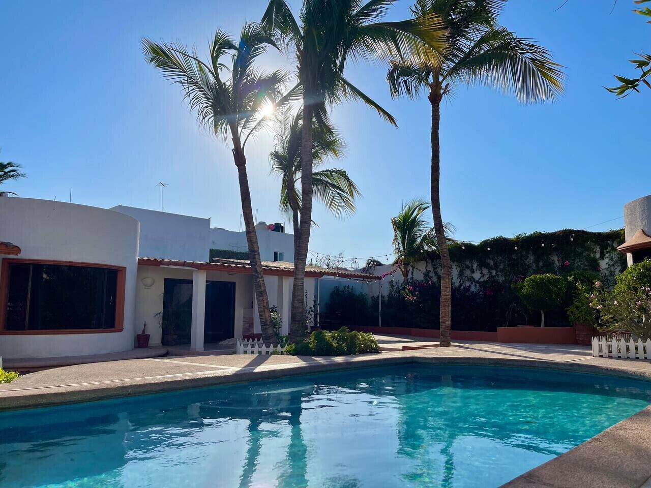 A swimming pool surrounded by palm trees and a white building with large windows.