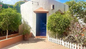 Um edifício branco com porta azul, cercado por uma cerca branca de piquete e vasos de plantas.