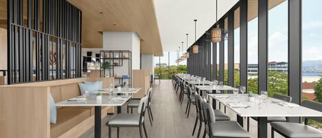 Un restaurante moderno con mesas y sillas largas, ventanas amplias y vistas a la ciudad.