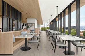 Un restaurant moderne avec de longues tables et des chaises, de grandes fenêtres et une vue sur la ville.