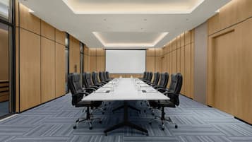A conference room with a long table, black chairs, and a projector screen.